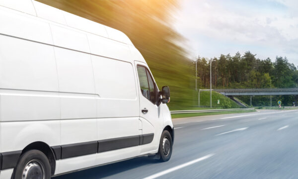 White modern delivery small shipment cargo courier van moving fast on motorway road to city urban suburb. Busines distribution and logistics express service. Mini bus driving on highway on sunny day.